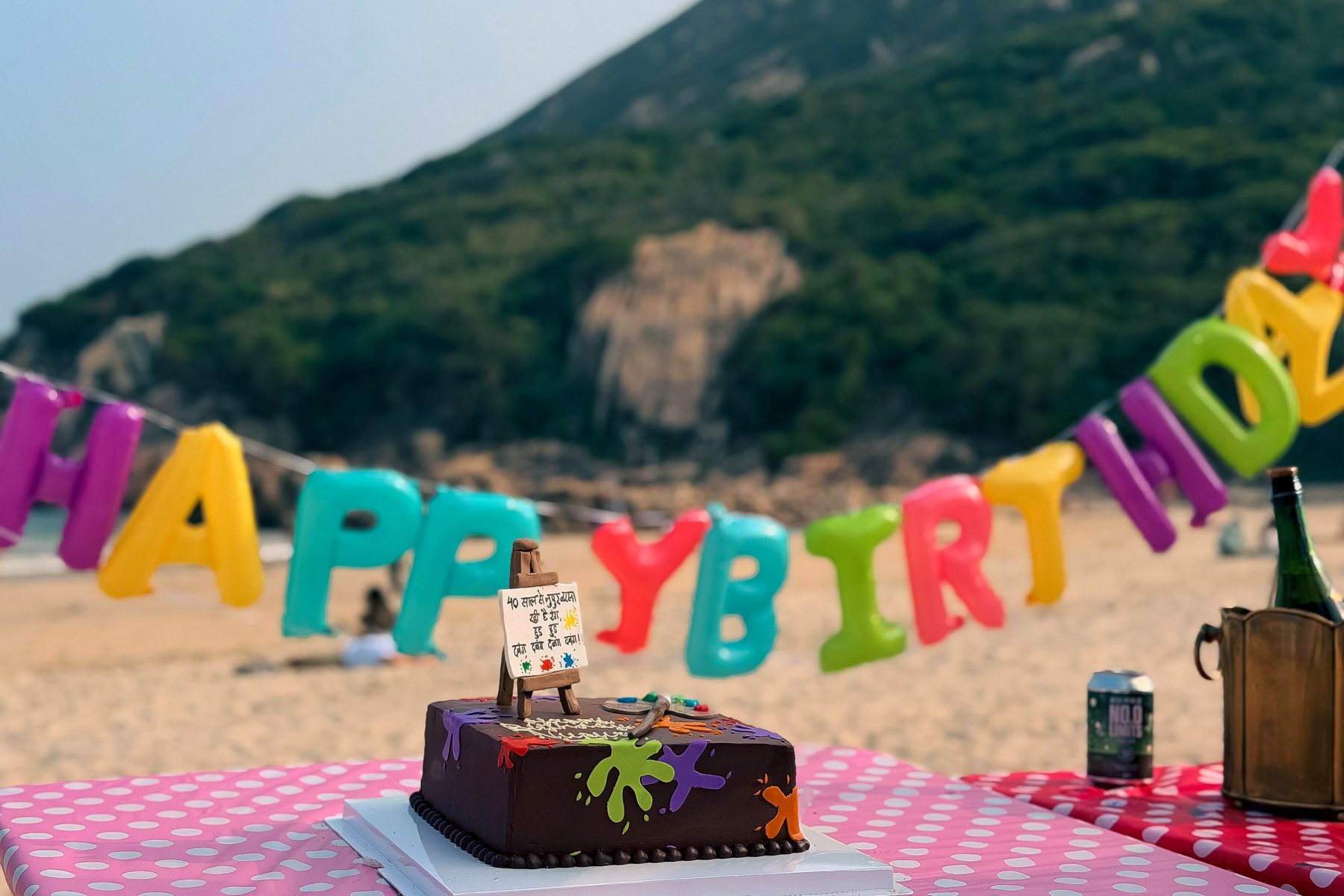 A decorated cake on a spotted cloth with HAPPY BIRTHDAY letters and the sea behind
